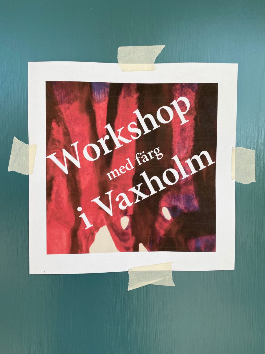 En papperslapp med skylten "Workshop med färg i Vaxholm" upptejpad på en dörr.