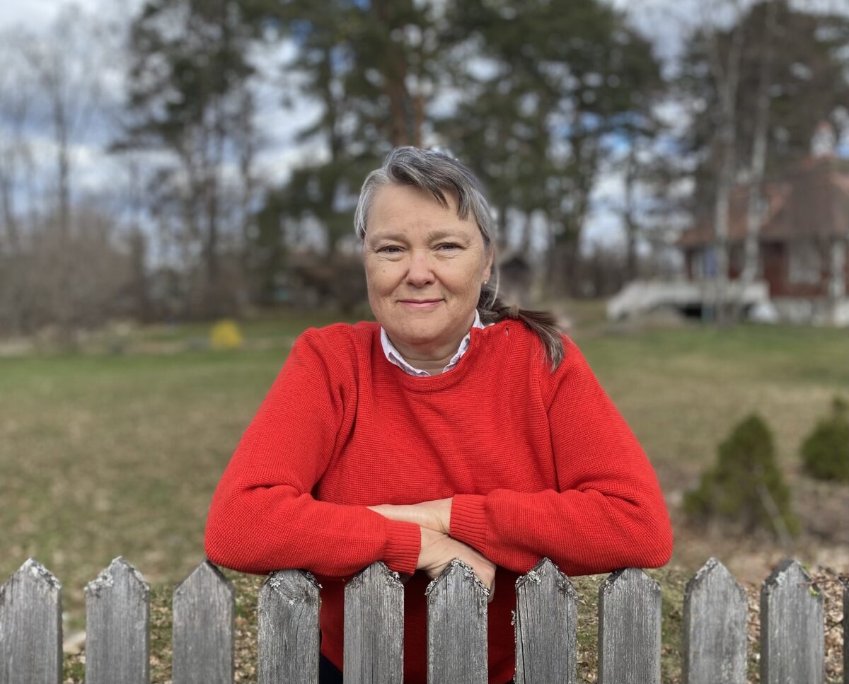 Camilla L. Kvissberg som står i en röd tröja vid ett gammalt staket.